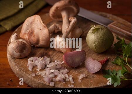 Artistic still life of mushrooms, shallots, tomatillos and parsley on old wood cutting board. Stock Photo