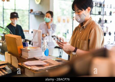 Women in protective face mask placing an order with cell phone at cafe counter Stock Photo