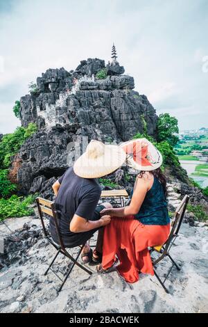 Couple of tourists kissing on the background of beautiful Vietnam, Tam Coc Ninh bin. Hiding behind conical traditional hats. Pagoda and landscape. Hol Stock Photo