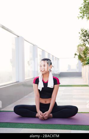 Young beautiful Asian woman sitting on yoga mat and smiling in morning. Sport and healthy lifestyle. Stock Photo