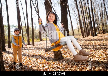 Outside the little boy push the little girl riding on the swing Stock Photo