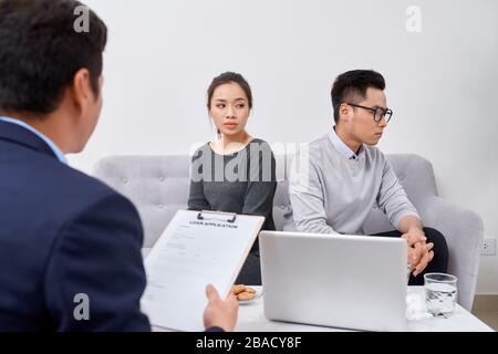 It is not my fault! Displeased young man talking to psychiatrist and gesturing while his wife sitting near him and keeping arms crossed Stock Photo