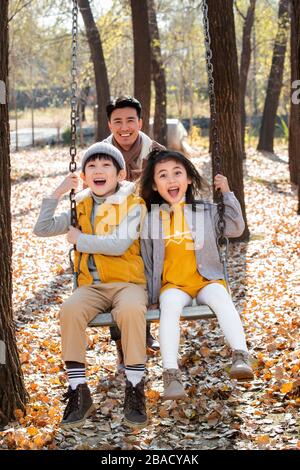 The happy children and father playing on the swings in the outdoor Stock Photo
