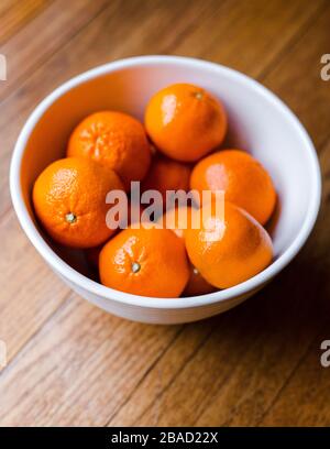 Delicious juicy oranges in a white bowl on a wooden background; close up view with soft natural lighting Stock Photo