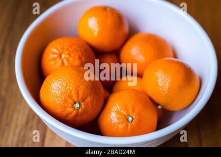 Oranges fruit in a white bowl on a wooden background close up macro Stock Photo