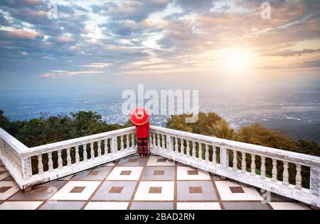 Woman with red Thai umbrella at view point looking at Chiang Mai city panorama at sunset in Thailand