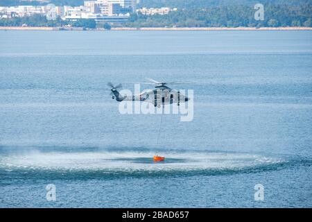 Hong Kong, China- February 23 2020: A Helicopter with a fire fighting water bucket fills up with water and flies away to fight a forest fire in Hong K Stock Photo