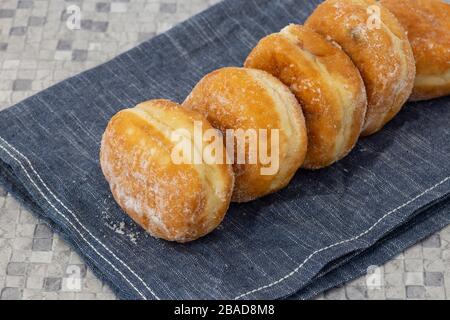 Jam doughnuts coated in icing sugar on a blue tea towel on a kitchen worktop.  Mosaic tile background Stock Photo