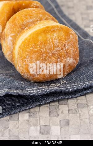 Jam doughnuts coated in icing sugar on a blue tea towel on a kitchen worktop.  Mosaic tile background Stock Photo