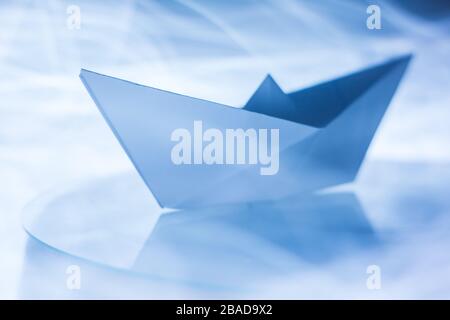 Paper boat splitting blue light trails symbolizing waves in the sea Stock Photo