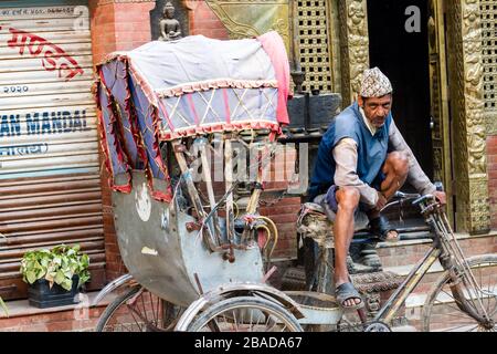 Kathmandu, Nepal - November 17, 2018: Rickshaw driver sitting near his rickshaw on Kathmandu street. Public transport in Nepal. Stock Photo