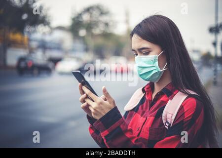 Asian Young woman using smart phone in the city wearing face mask because of air pollution, particulates and for protection flu virus, influenza, coro Stock Photo