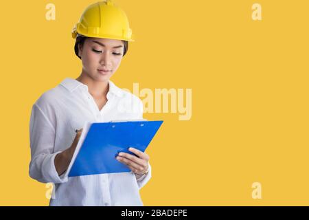 Asian women engineering inspecting and working and holding blueprints on yellow background Stock Photo