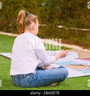 Stress relief with art therapy. Teenager girl paints a paper house template with colorful watercolors in the garden. Kid being homeschooled due to school shut down during corona virus pandemic. Stock Photo