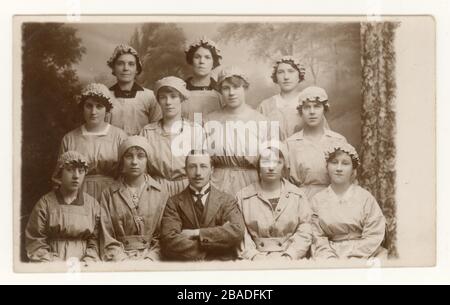 Original WW1 era studio portrait postcard of group of civilian female munitions workers with manager, one of the girls is wearing an 'On War Service' badge, England, Britain, U.K. Circa 1916, 1917 or  1918