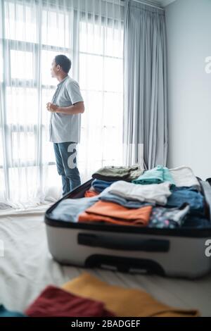 young man wearing clothes after opening his suitcase in the bedroom after checking in at the hotel Stock Photo