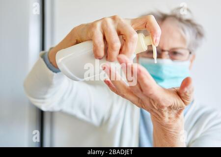 Elderly elderly woman with mouth protection uses hand cream for skin care during coronavirus epidemic Stock Photo
