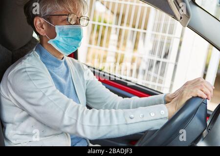 Elderly woman driving a car with face mask during Covid-19 epidemic Stock Photo