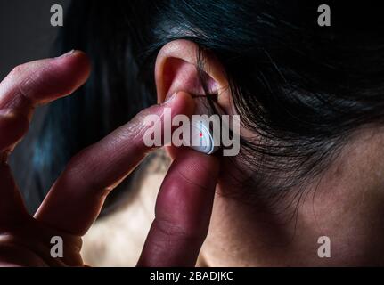 Fingers holding white wireless earbud on woman ear Stock Photo