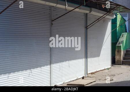 Closed local daily market. Three small shops are closed with white shutters. Empty street market in the daytime. A clear sunny day. Without people. Stock Photo