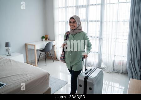 beauty young hijab traveler walk and carrying her bag and holding suitcase in the front windows with curtain Stock Photo