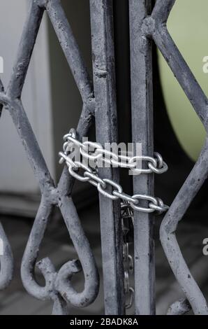 Metal chain on lattice gate. The black gate of the mansion is closed from the inside by a padlock and a chain. Limited access. Selective focus. Stock Photo