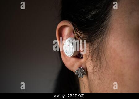 White wireless earbud in woman ear with four leaf clover earring Stock Photo