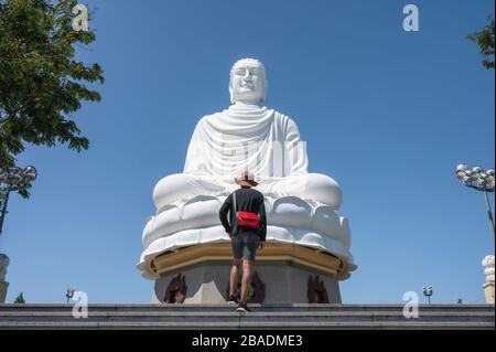 Man tourist standing on stairs with big buddha and blue sky in Long Son pagoda temple at Nha Trang, Vietnam Stock Photo