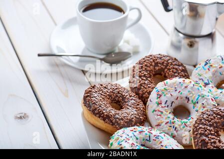 Closeup photo of sweet breakfast or snacks. Chocolate donuts and cup of coffee. White wooden table top with space for text. Stock Photo