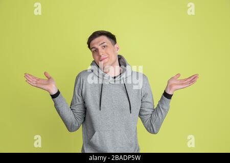 Doesn't know, uncertain. Caucasian man's portrait isolated on yellow studio background. Freaky male model in casual clothes. Concept of human emotions, facial expression, sales, ad. Unusual appearance. Stock Photo