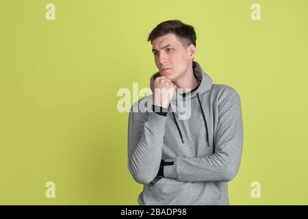 Thinking, dreamful. Caucasian man's portrait isolated on yellow studio background. Freaky male model in casual clothes. Concept of human emotions, facial expression, sales, ad. Unusual appearance. Stock Photo