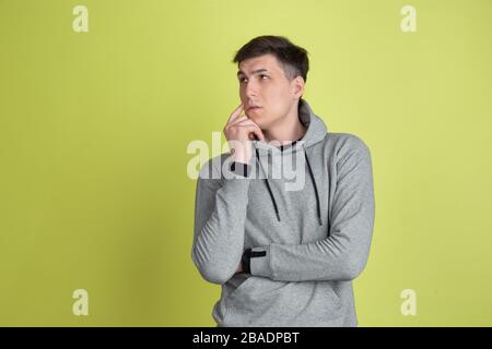 Thinking, dreamful. Caucasian man's portrait isolated on yellow studio background. Freaky male model in casual clothes. Concept of human emotions, facial expression, sales, ad. Unusual appearance. Stock Photo