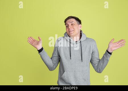 Doesn't know, uncertain. Caucasian man's portrait isolated on yellow studio background. Freaky male model in casual clothes. Concept of human emotions, facial expression, sales, ad. Unusual appearance. Stock Photo