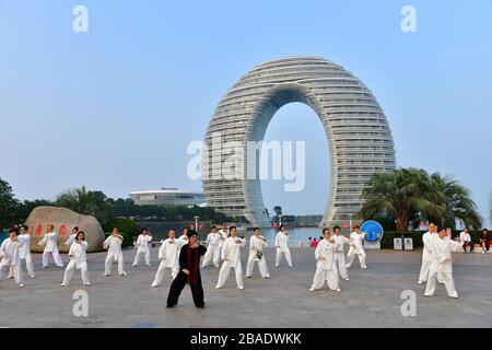 Huzhou, China, October 2019; Large group of people practicing Tai Chi, Yang style, on the shore of Tai Lake with the iconic horseshoe shaped hotel in Stock Photo