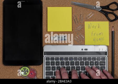 Work home quarantine concept POV with mobile computer. Hands typing on a portable keyboard next to a tablet, with a USB stick and yellow notes papers. Stock Photo