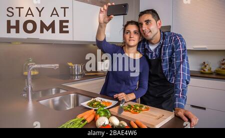 Couple in kitchen cooking and taking selfie with smartphone Stock Photo