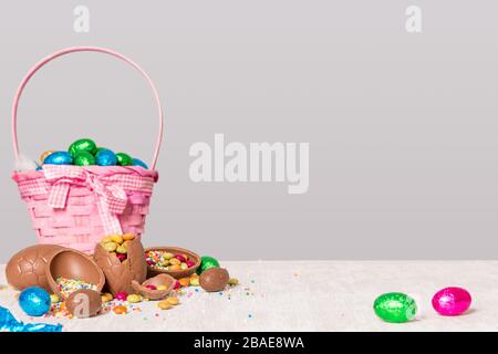 chocolate easter eggs in a basket and on wooden table top with multi colored sprinkles and sweets spilling out over the table - easter holiday concept Stock Photo