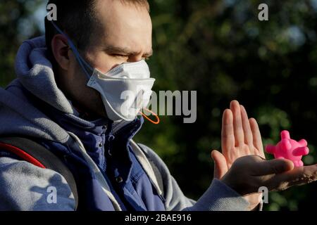 Young Man in Protective Mask Stops the Corona Virus and Pandemic Covid-19. A Man holding the icon of the Corona Virus in his Hand Stock Photo