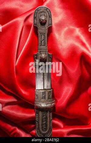 Beautiful example of caucasian dagger with blade in form of Rome sword on red silk background. 19th century (Time of Russian-Caucasian wars (1816-1864 Stock Photo