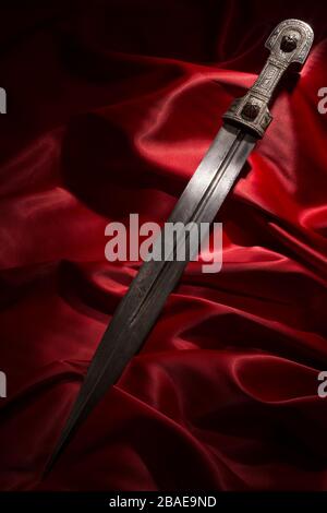 Beautiful example of caucasian dagger with blade in form of Rome sword on red silk background. 19th century (Time of Russian-Caucasian wars (1816-1864 Stock Photo