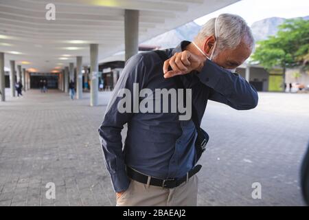 Middle aged man wearing mask against Coronavirus Covid 19 coughing into elbow Stock Photo
