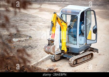 Tracked mini excavator breaks out old curbs before installing new curbs. The concept of using economical and compact equipment for urban needs. Stock Photo