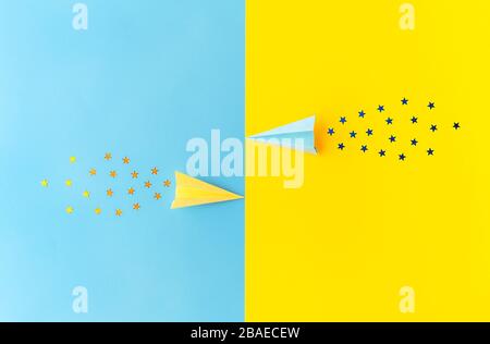 Top view of yellow and blue paper planes with star shaped confetti trails on blue and yellow background. Minimalist flat lay image with copy space. Fe Stock Photo