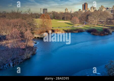 Central park in NYC daylight view in winter wide angle view with frozen lake, people walking, skylines and clouds in the sky in background Stock Photo