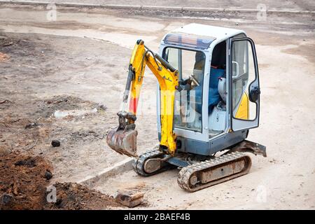 Tracked mini excavator breaks out old curbs before installing new curbs. The concept of using economical and compact equipment for urban needs. Stock Photo