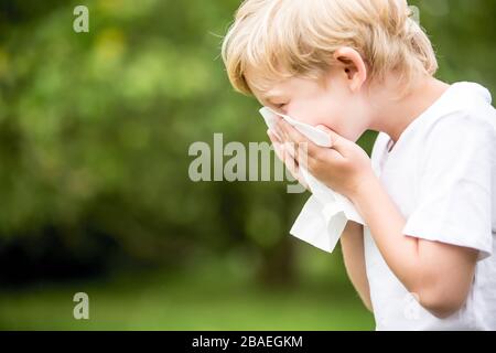 Child with allergy in nature while sneezing into a handkerchief Stock Photo