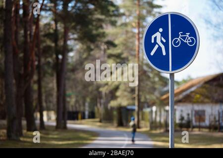 Bicycle and pedestrian shared route road sign over out of focus background of road in park surrounded by forest and houses Stock Photo