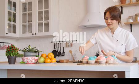 Young woman decorating cupcakes in bright kitchen Stock Photo