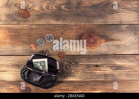 Open black leather pocket wallet with coins one cent, quarter dollar and 2 dollars banknote nearby. Financial crisis, poverty, lack money. On wooden b Stock Photo