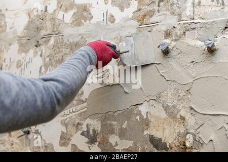 construction worker applying plaster on the old bathroom wall with spatula Stock Photo